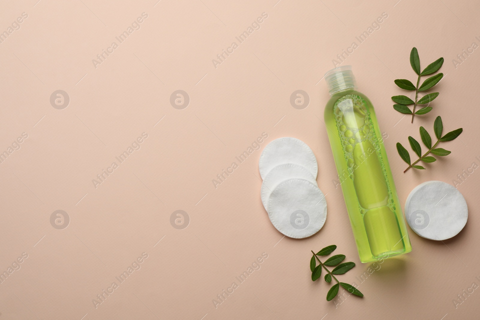 Photo of Cotton pads, leaves and makeup removal product on beige background, flat lay. Space for text