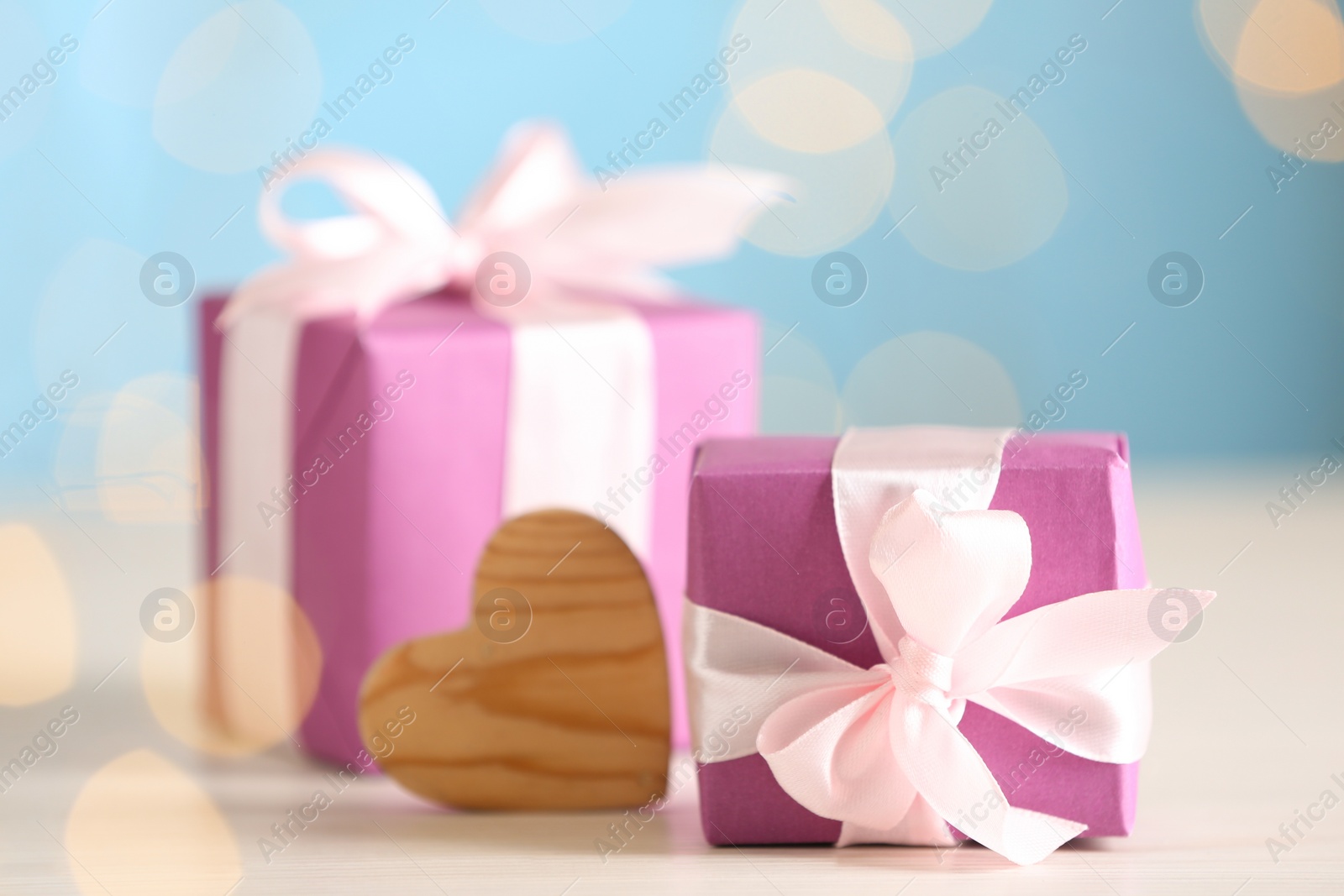 Photo of Beautiful gift boxes and decorative heart on light wooden table, closeup. Valentine's Day celebration