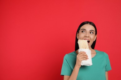 Photo of Young woman eating delicious shawarma on red background. Space for text