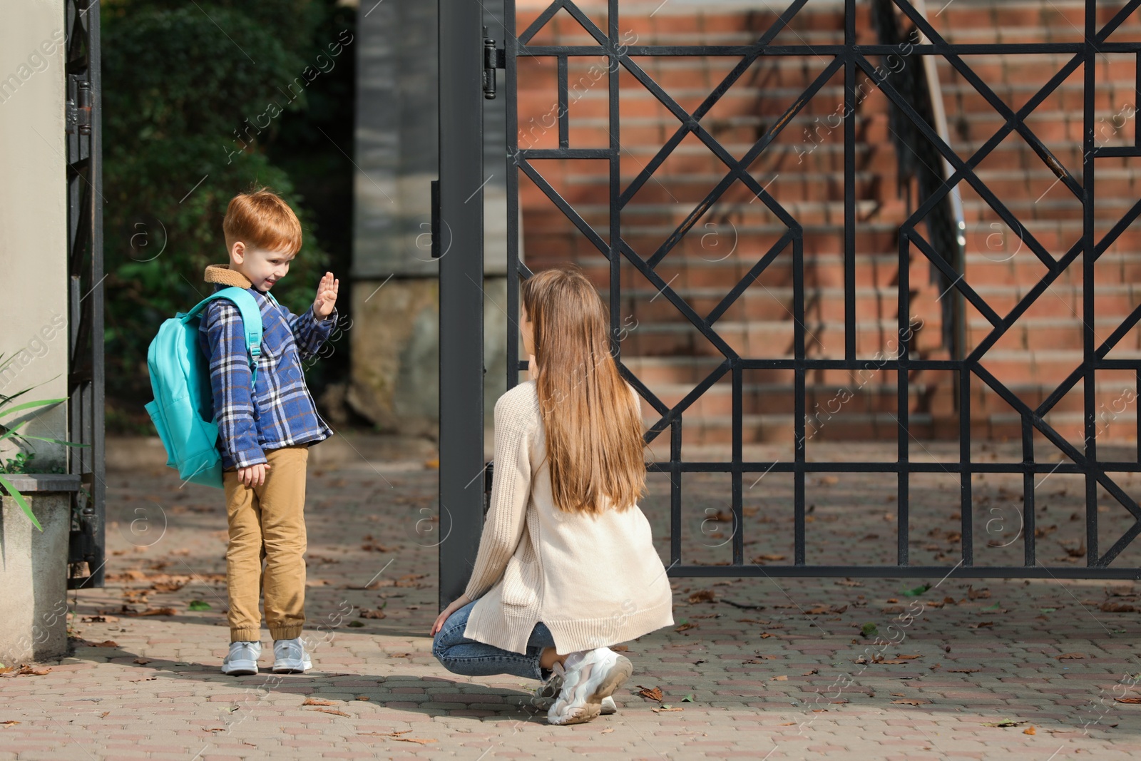 Photo of Little boy waving goodbye to his mother near school