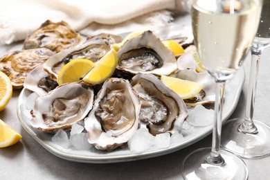 Photo of Fresh oysters with lemon and glasses of champagne on grey table, closeup