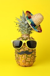 Photo of Pineapple with Mexican sombrero hat, sunglasses and fake mustache on yellow background