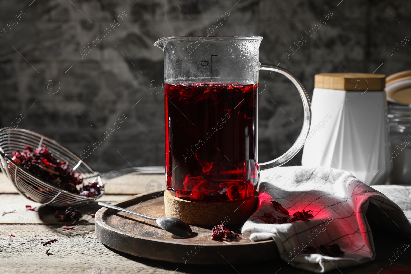 Photo of Freshly brewed hibiscus tea in teapot and dry flower petals on wooden table