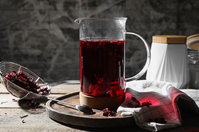 Photo of Freshly brewed hibiscus tea in teapot and dry flower petals on wooden table