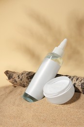 Photo of Cosmetic products and tree bark on sand against beige background