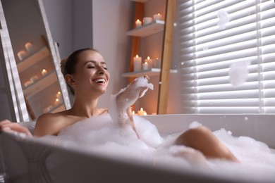 Beautiful woman taking bath in tub with foam indoors