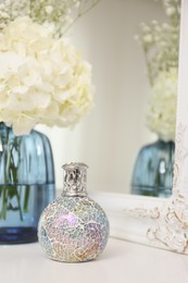 Photo of Stylish catalytic lamp with beautiful bouquet on white table near mirror. Cozy interior