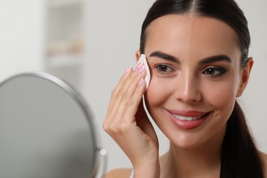 Beautiful woman removing makeup with cotton pad indoors