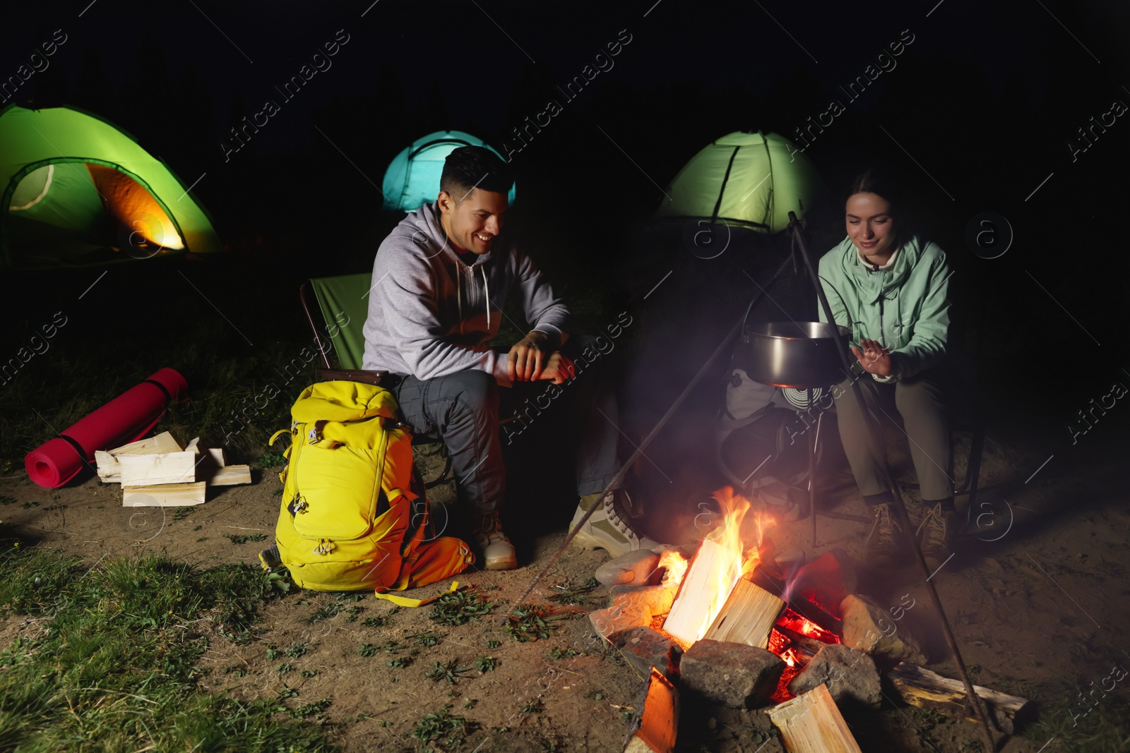 Photo of Couple sitting near bonfire in camp at night