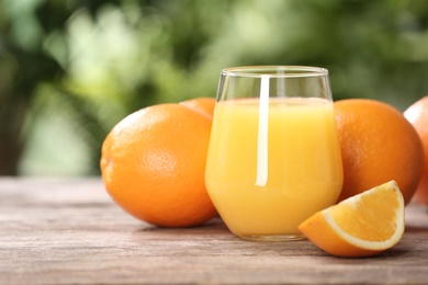 Photo of Glass of fresh juice and oranges on wooden table. Space for text