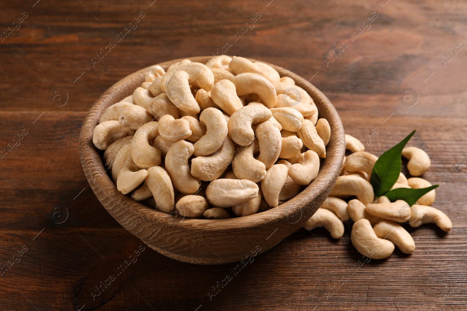 Photo of Tasty cashew nuts in bowl on wooden table