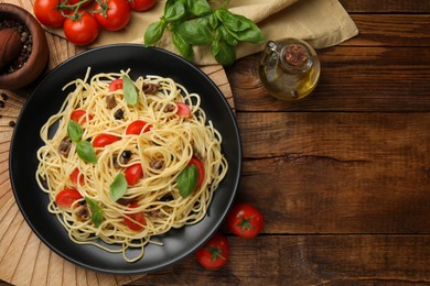 Photo of Delicious pasta with anchovies, tomatoes and basil on wooden table, flat lay. Space for text