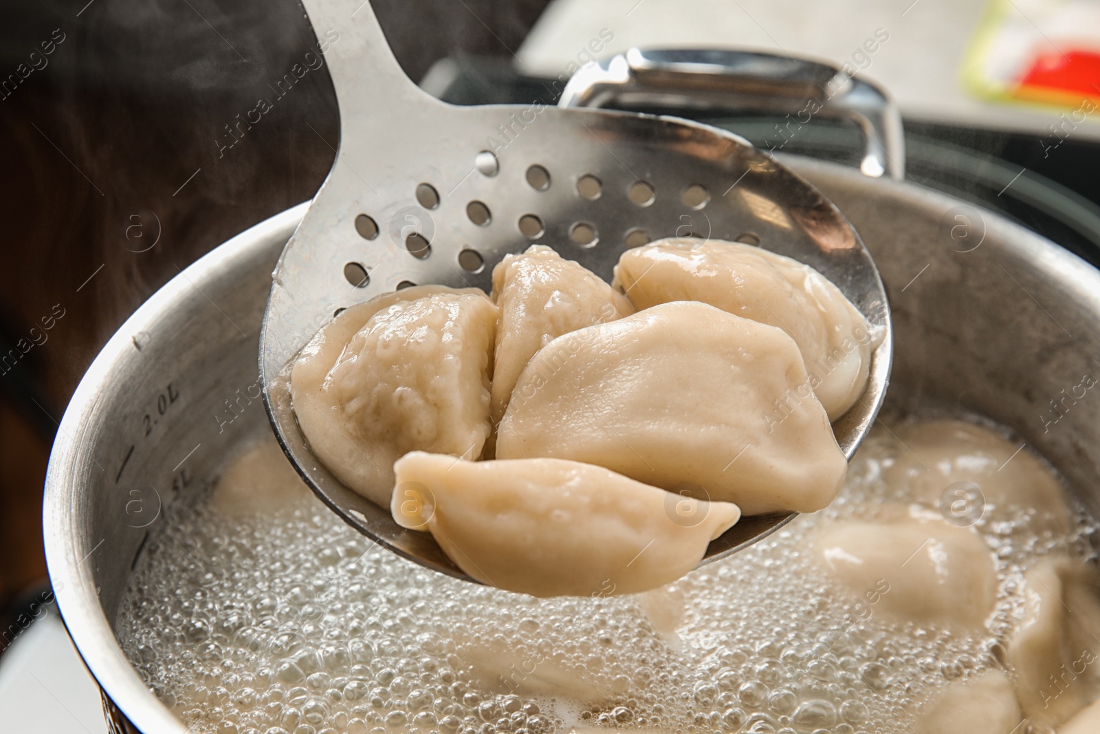 Photo of Closeup of dumplings on skimmer over stewpan with boiling water. Home cooking