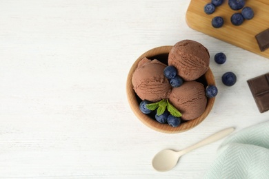 Flat lay composition with bowl of chocolate ice cream and blueberries on white wooden table, space for text