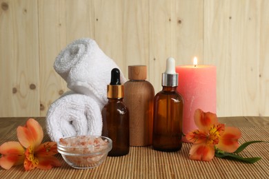 Photo of Aromatherapy. Essential oil in bottles, candle, sea salt, flowers and towel on bamboo mat