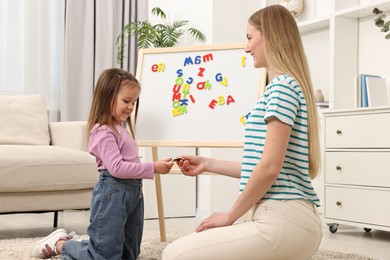 Mom teaching her daughter alphabet with magnetic letters at home