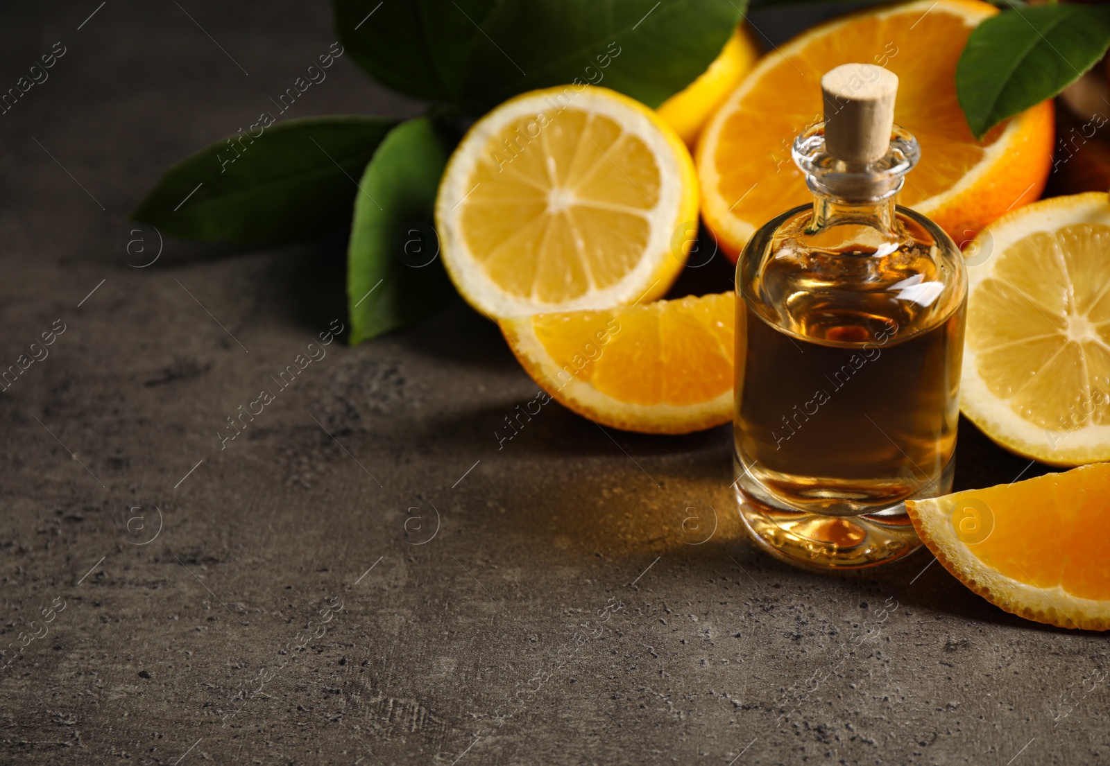 Photo of Bottle of essential oil and citrus fruits on grey table. Space for text