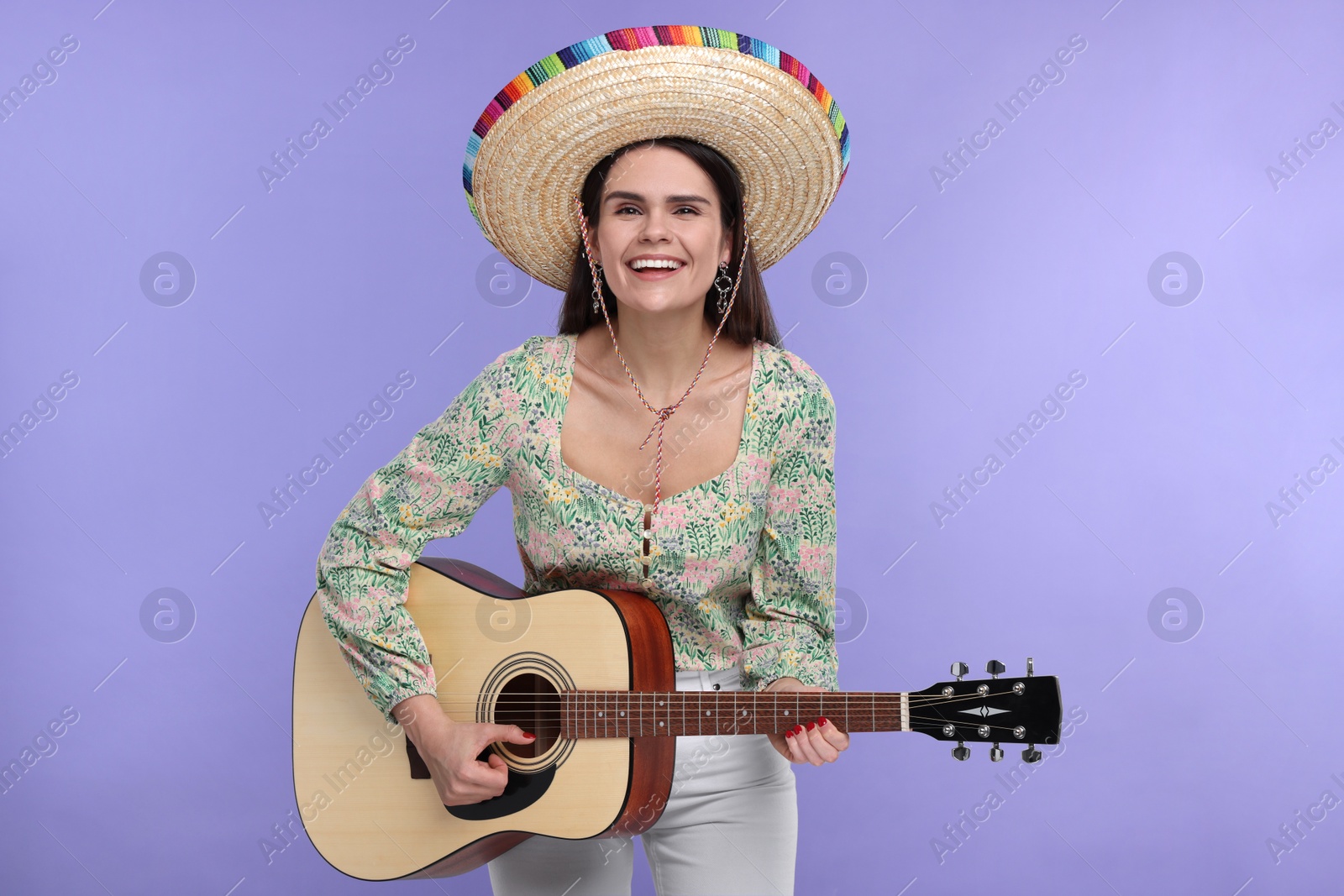 Photo of Young woman in Mexican sombrero hat playing guitar on violet background