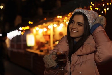 Woman with glass cup of mulled wine at winter fair. Space for text