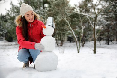 Photo of Young woman making snowman outdoors on winter day. Space for text