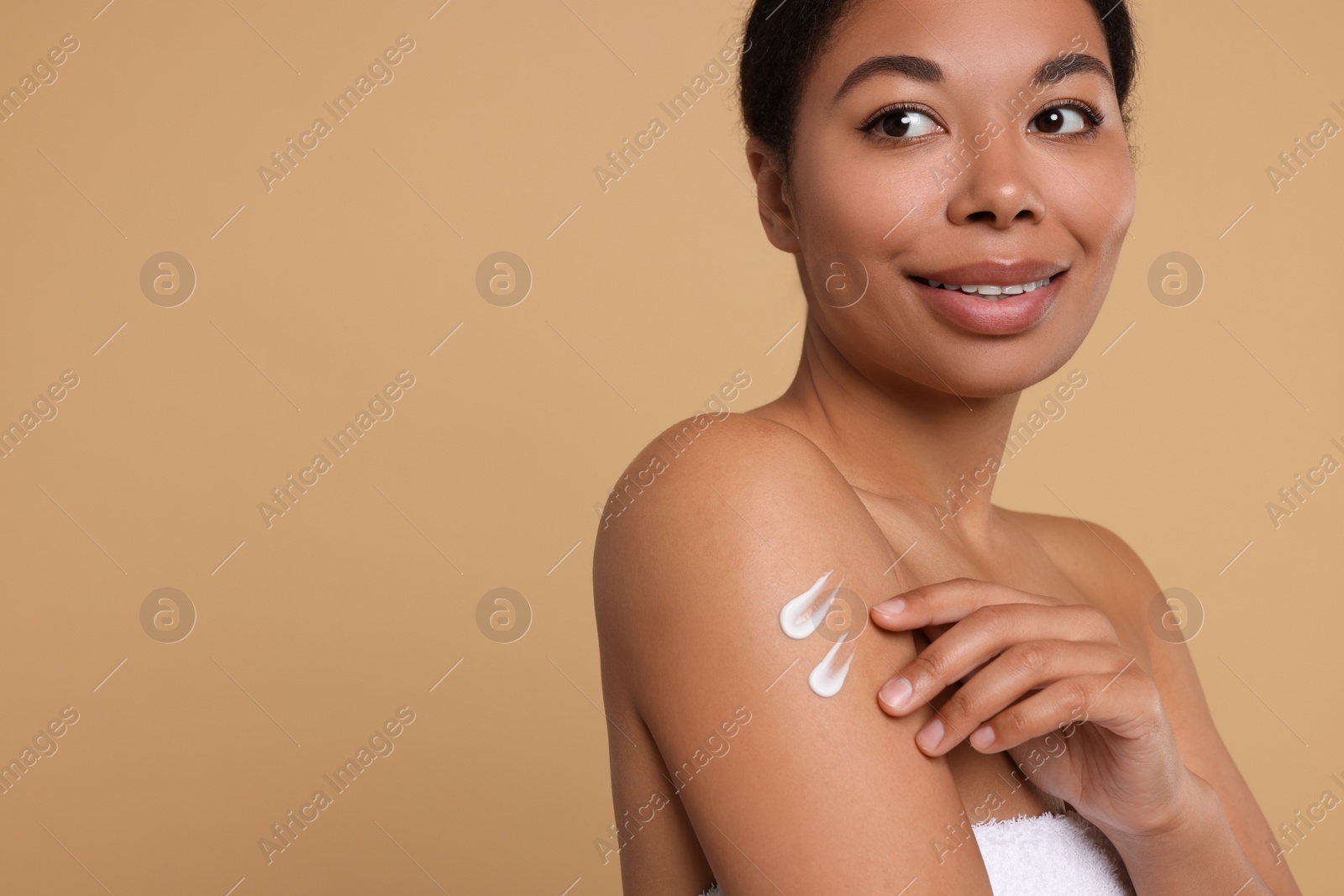 Photo of Young woman applying body cream onto shoulder on beige background. Space for text