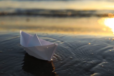 Photo of White paper boat in shallow water of sea at sunset, space for text