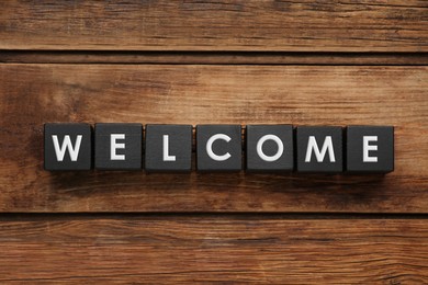 Word Welcome made of black cubes on wooden background, top view