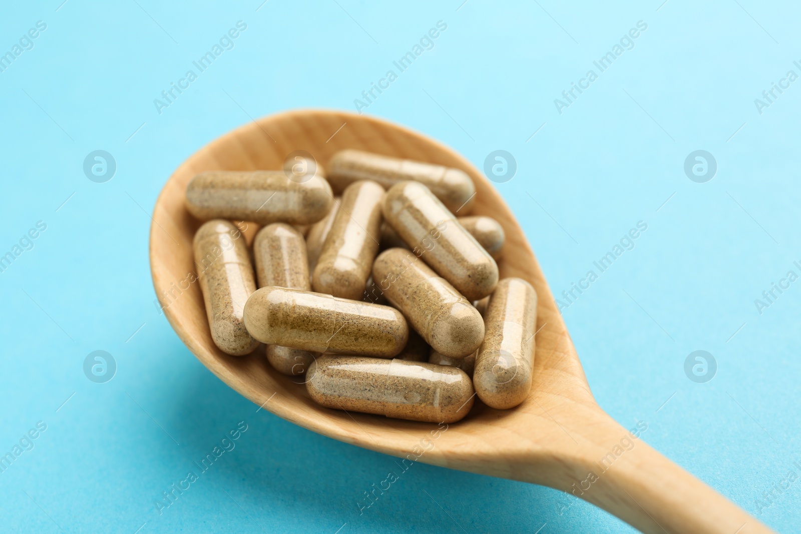 Photo of Vitamin capsules in wooden spoon on light blue background, closeup