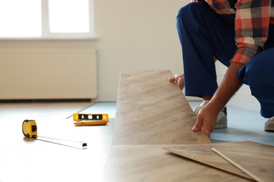 Photo of Professional worker installing new parquet flooring indoors, closeup