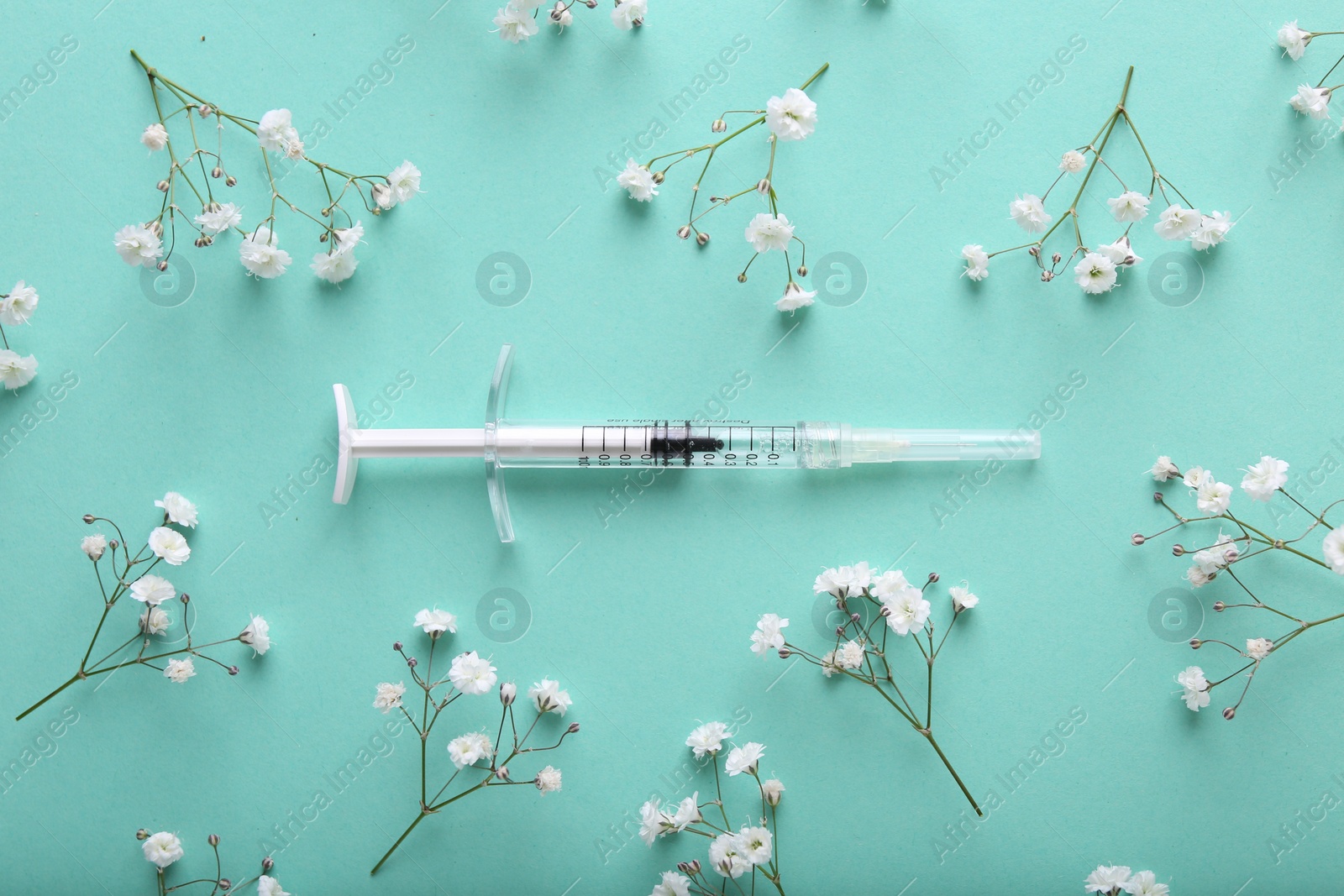 Photo of Cosmetology. Medical syringe and gypsophila flowers on turquoise background, flat lay