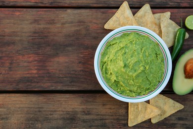 Delicious guacamole made of avocados, nachos and green pepper on wooden table, flat lay. Space for text