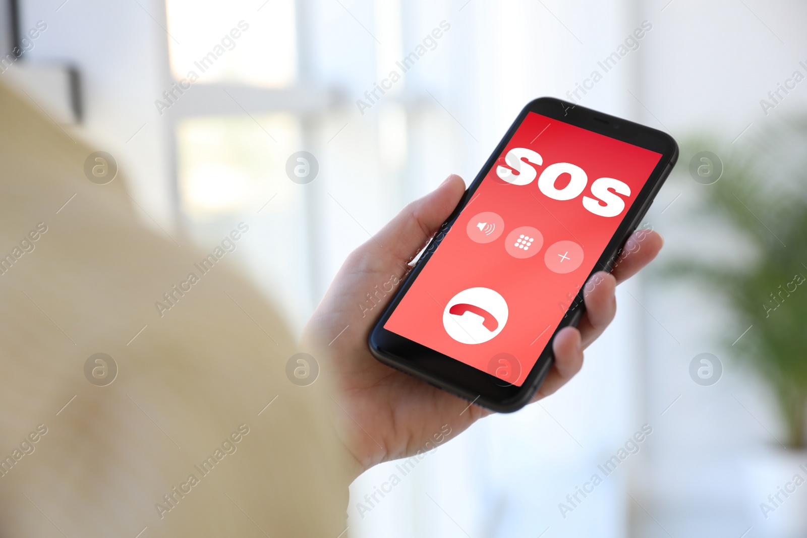 Image of Woman holding smartphone with emergency call SOS on screen indoors, closeup