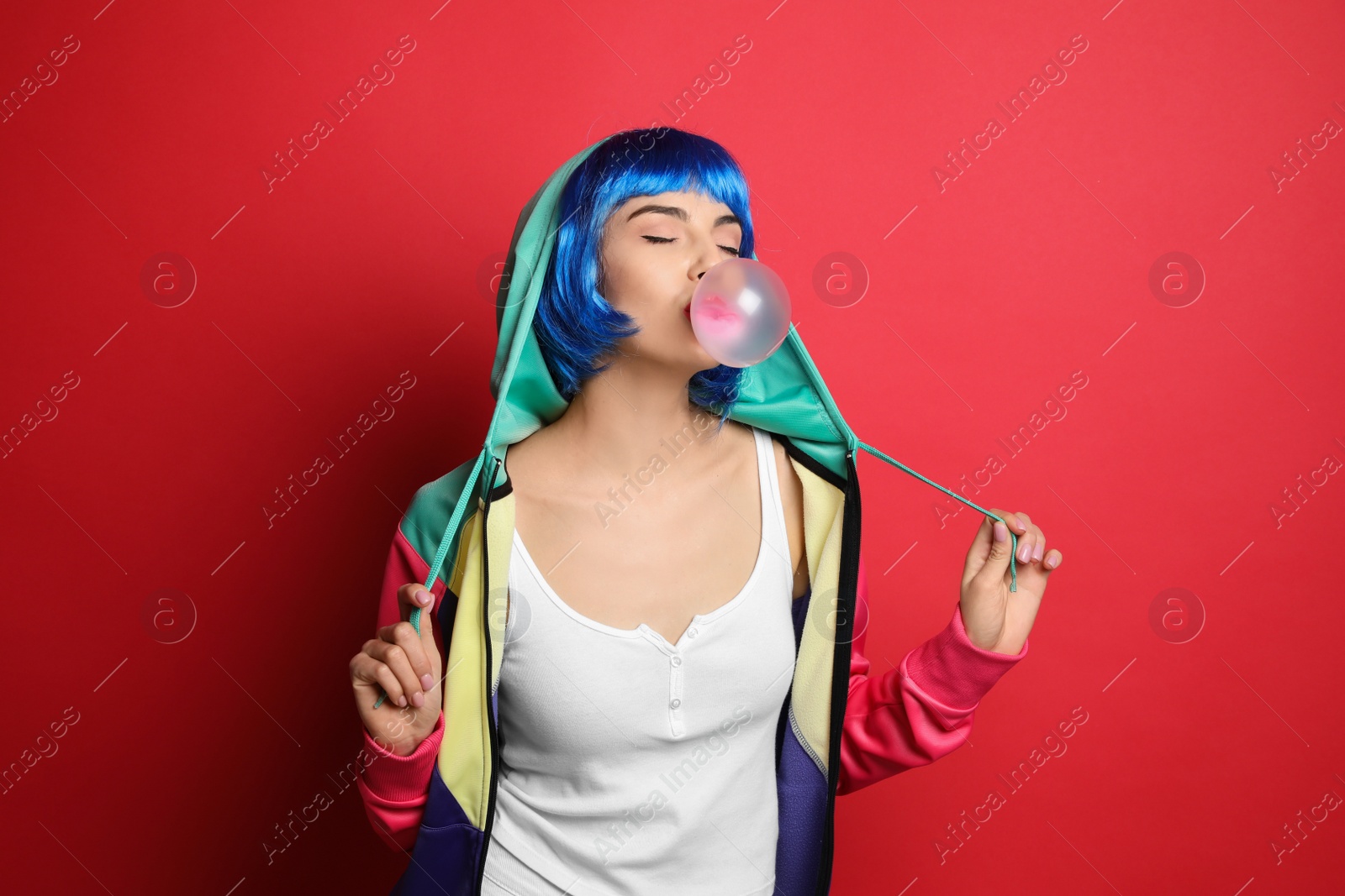 Photo of Fashionable young woman in colorful wig blowing bubblegum on red background