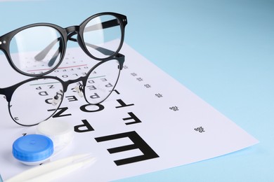 Photo of Vision test chart, glasses, lenses and tweezers on light blue background, closeup