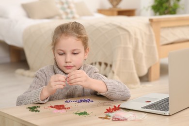 Photo of Little girl learning to make beaded jewelry with online course at home. Time for hobby