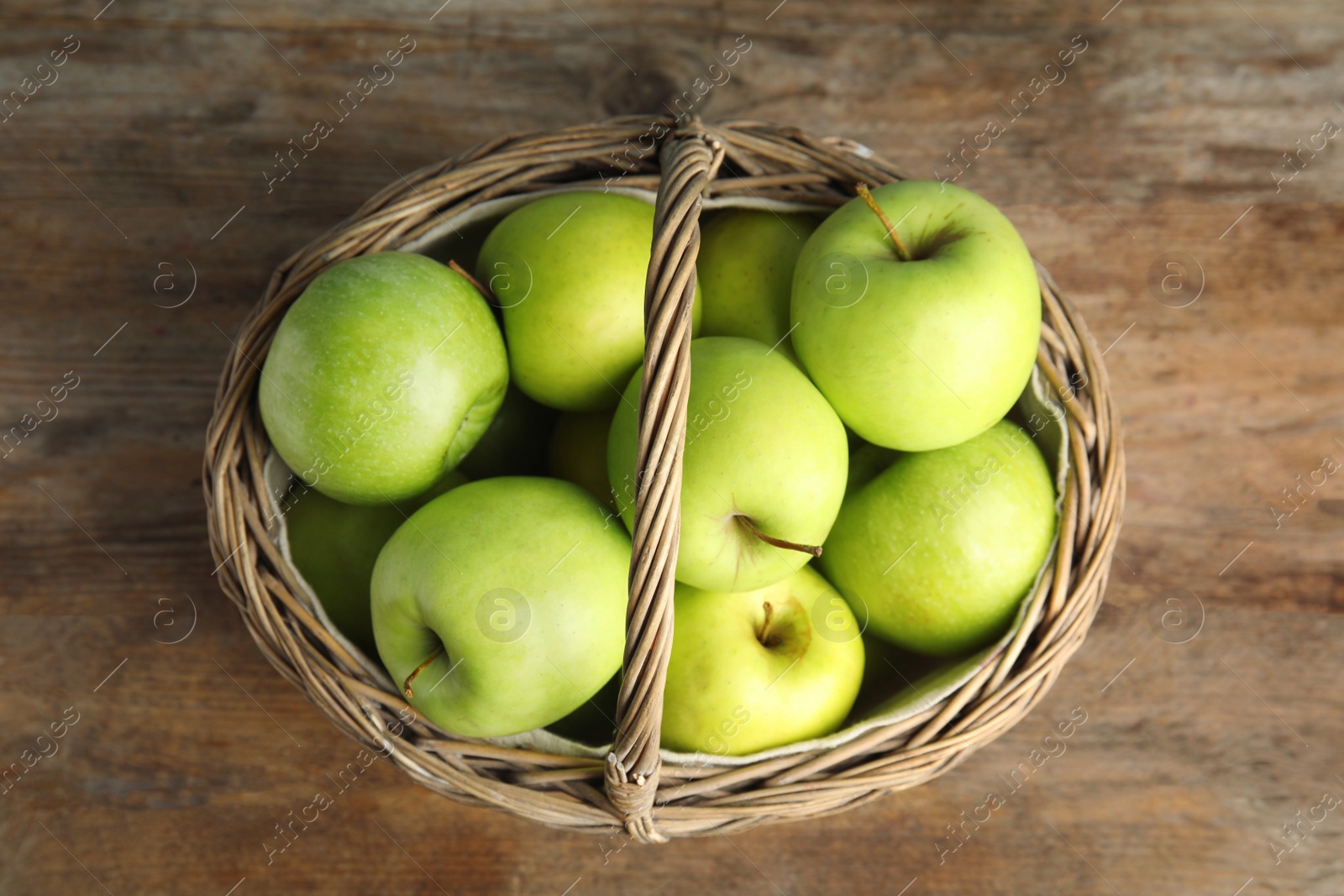 Photo of Wicker basket of fresh ripe green apples on wooden table, top view