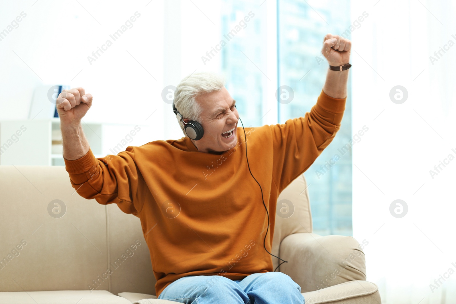 Photo of Portrait of mature man with headphones on sofa indoors