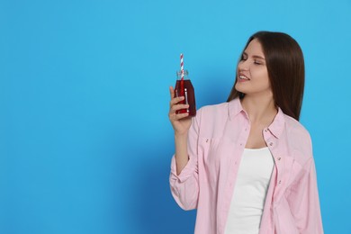 Beautiful young woman with glass bottle of juice on light blue background. Space for text