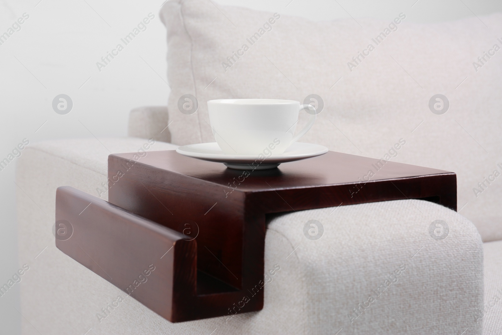 Photo of Cup of coffee on sofa with wooden armrest table indoors. Interior element