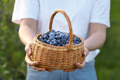 Photo of Woman with wicker basket of fresh blueberries outdoors, closeup. Seasonal berries
