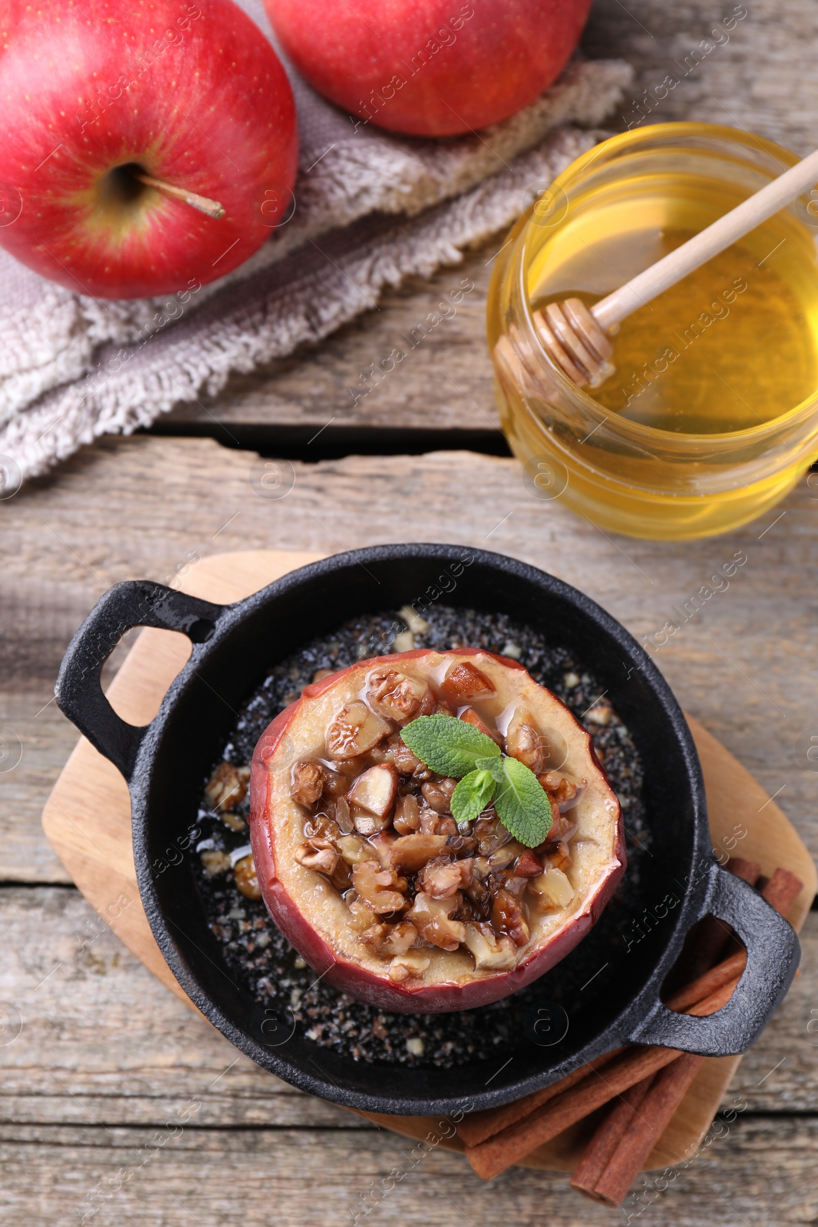 Photo of Tasty baked apple with nuts, honey and mint in baking dish on wooden table, flat lay