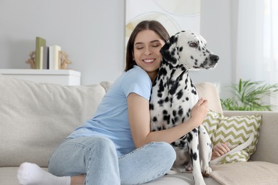 Beautiful woman hugging her adorable Dalmatian dog on sofa at home. Lovely pet