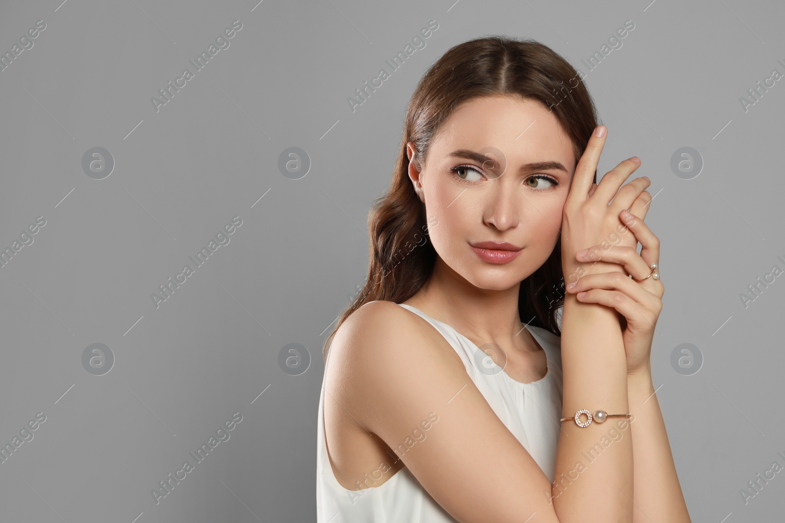 Photo of Young woman wearing elegant pearl jewelry on grey background, space for text