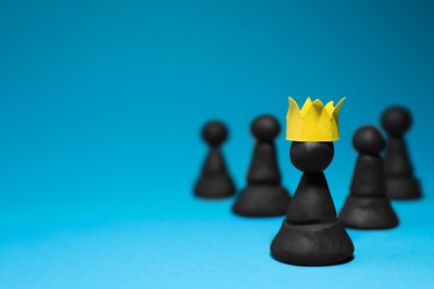 Photo of Black plasticine chess pieces and one with paper crown on light blue background, space for text