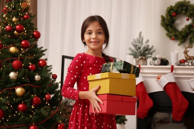Photo of Cute child with gift boxes near Christmas tree at home