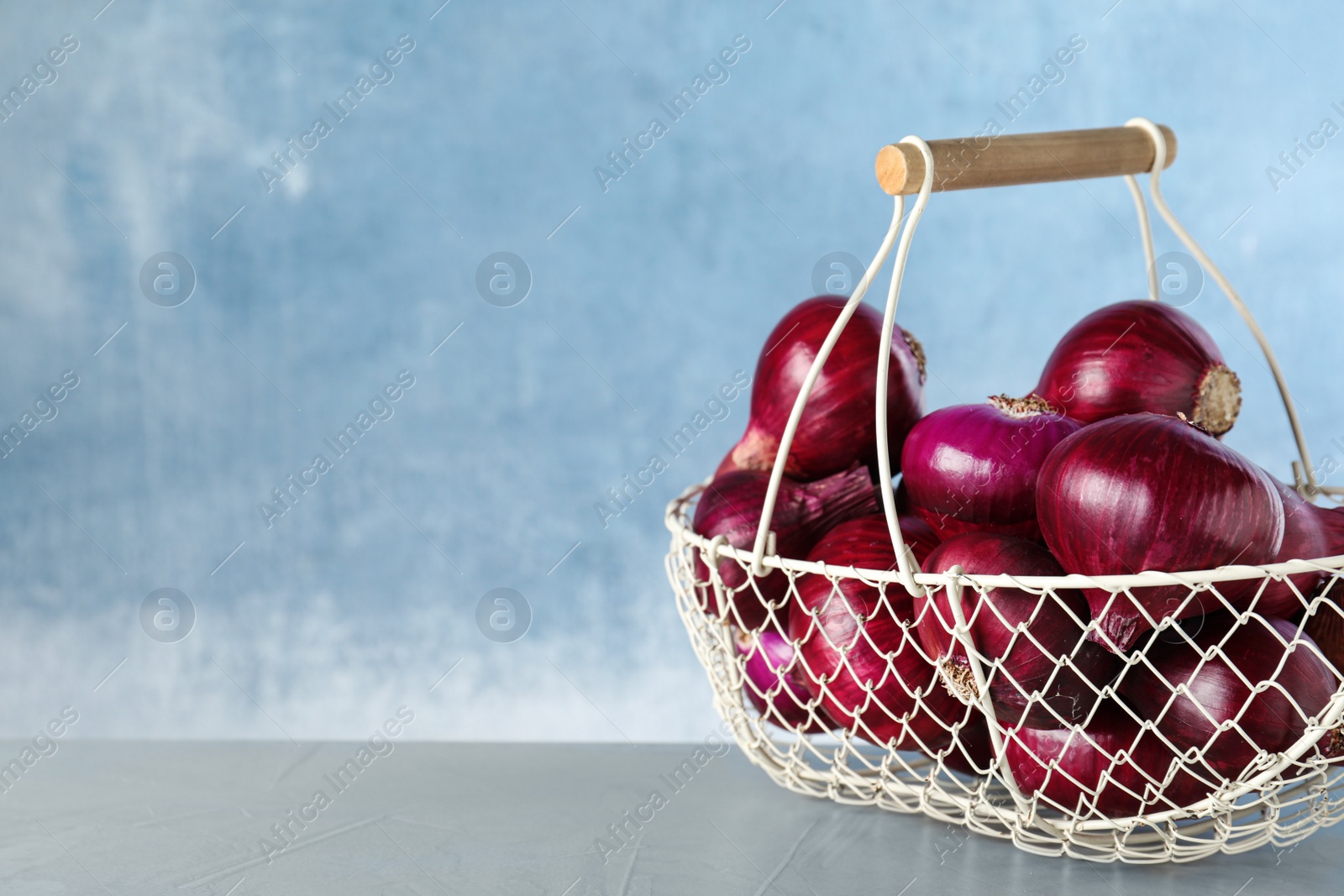 Photo of Metal basket with red onions on grey table, space for text