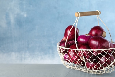 Metal basket with red onions on grey table, space for text