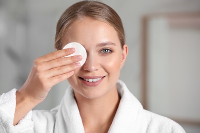 Beautiful young woman with cotton pad indoors