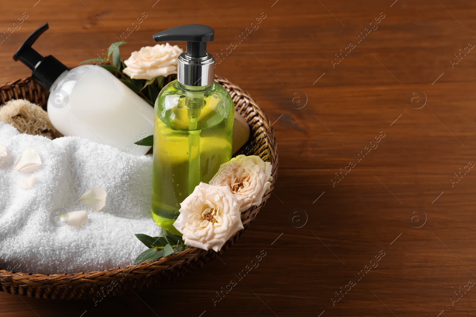 Photo of Dispensers of liquid soap, towel and roses in wicker basket on wooden table