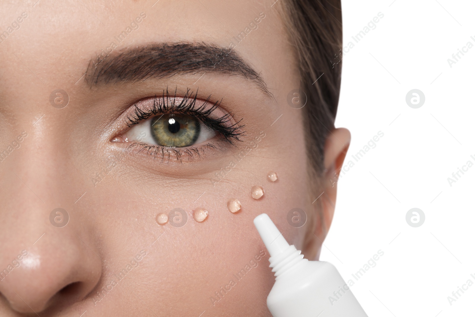 Photo of Young woman applying cream under eyes on white background, closeup